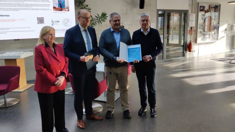 Gruppenfoto mit Föderurkunde. Vier Personen stehen nebeneinander in der Mitte Staatssekretär Hauer und ETOS-Sprecher Waldvogel